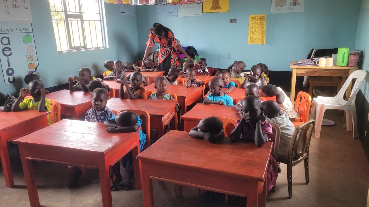 Nursery class at Hope Bridge, kids at red desks with the vowel chart on the wall