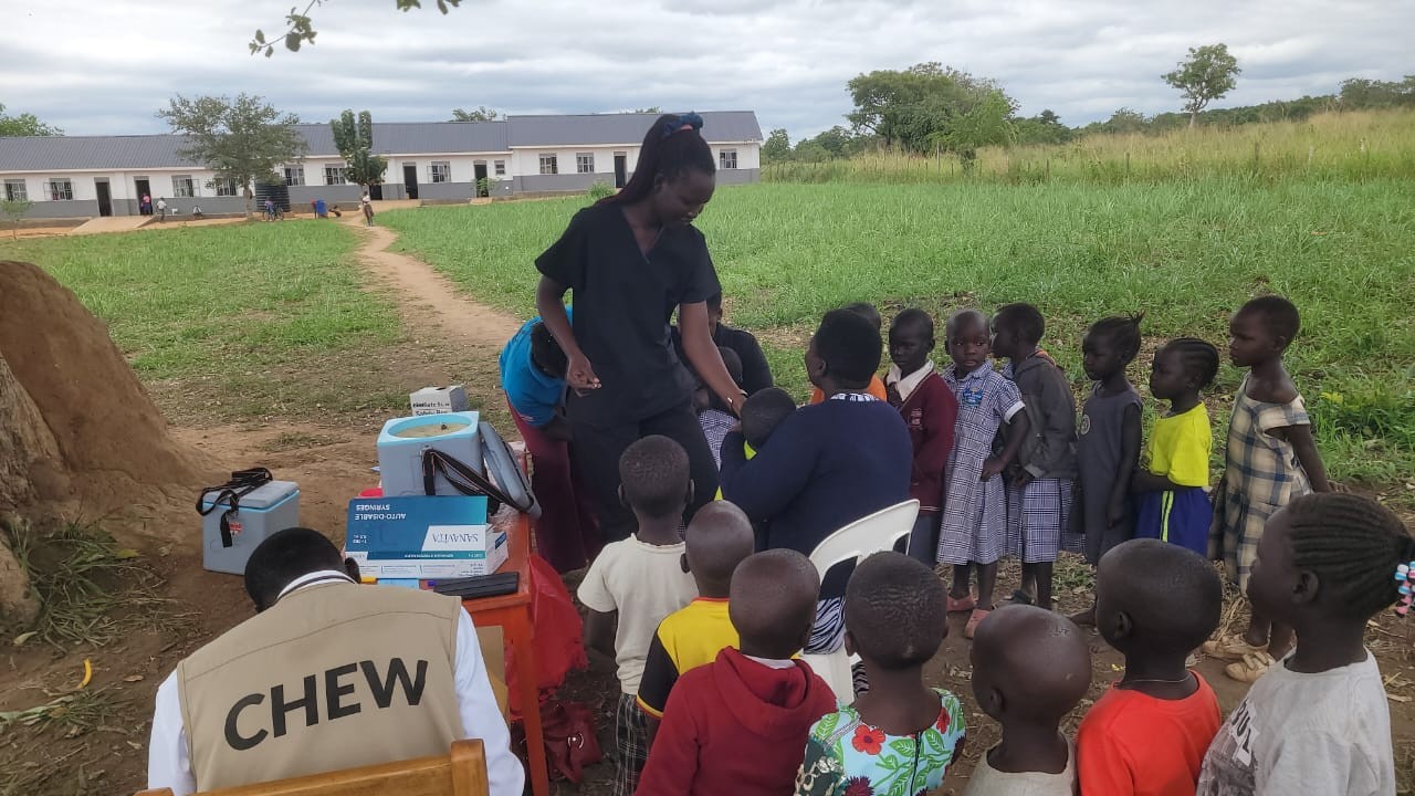 Community health workers vaccinating children under a tree at Hope Bridge